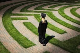 A woman in academic regalia walks a labyrinth