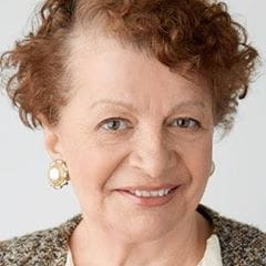 Woman with short red hair and pearl earrings smiling.
